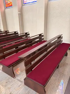 Bordowe poduszki siedziskowe w ciemnych ławkach przy jasnej ścianie kościoła