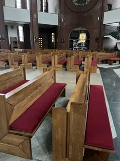 Drewniane ławki z bordowymi siedziskami we wnętrzu ceglanego kościoła