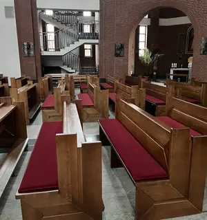 Widok między rzędami drewnianych ławek z bordowymi poduszkami